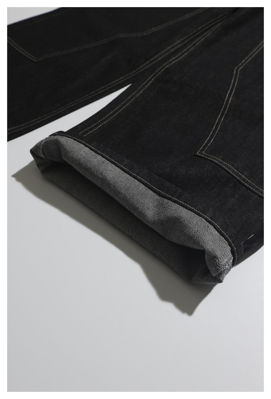 Close-up of a turned-up black denim hem with contrasting double stitching.