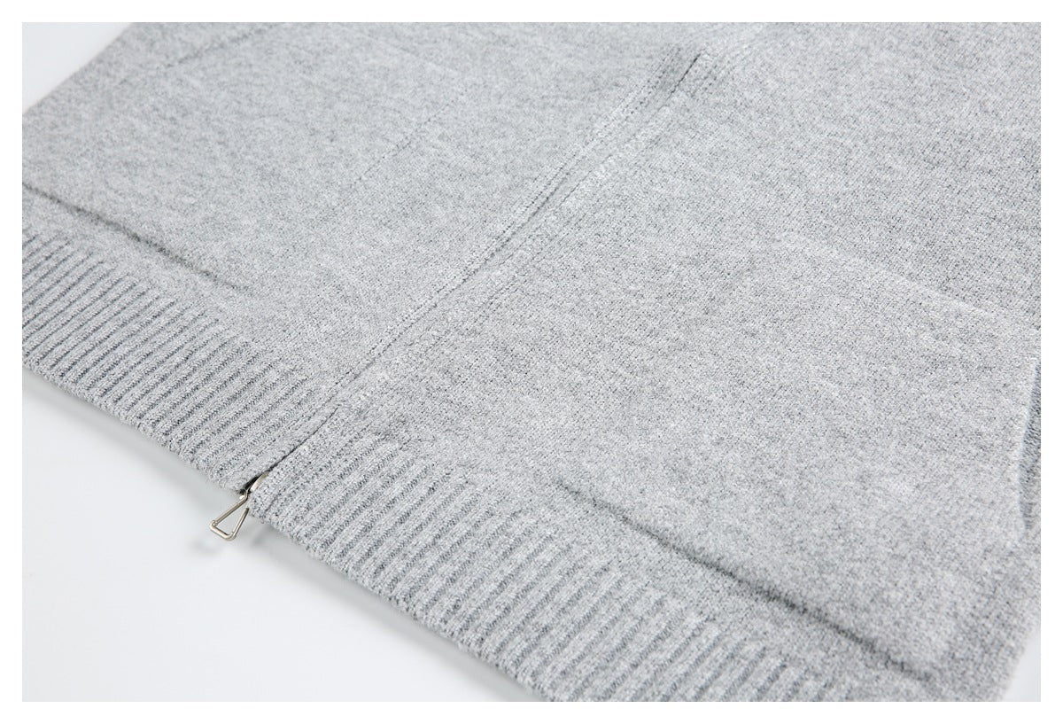 Close-up of a light gray knit garment with a ribbed edge and small metal zipper pull.
