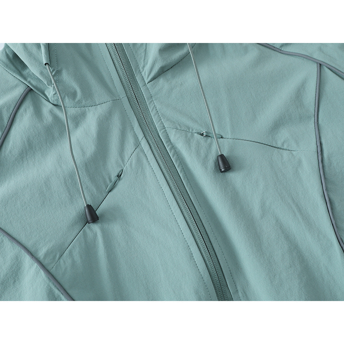 Close-up of the pale aqua jacket front, highlighting its zipper, drawcords, piping and zippered pockets.
