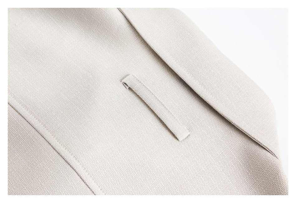 Close-up of a light beige blazer lapel and narrow welt pocket in textured fabric.