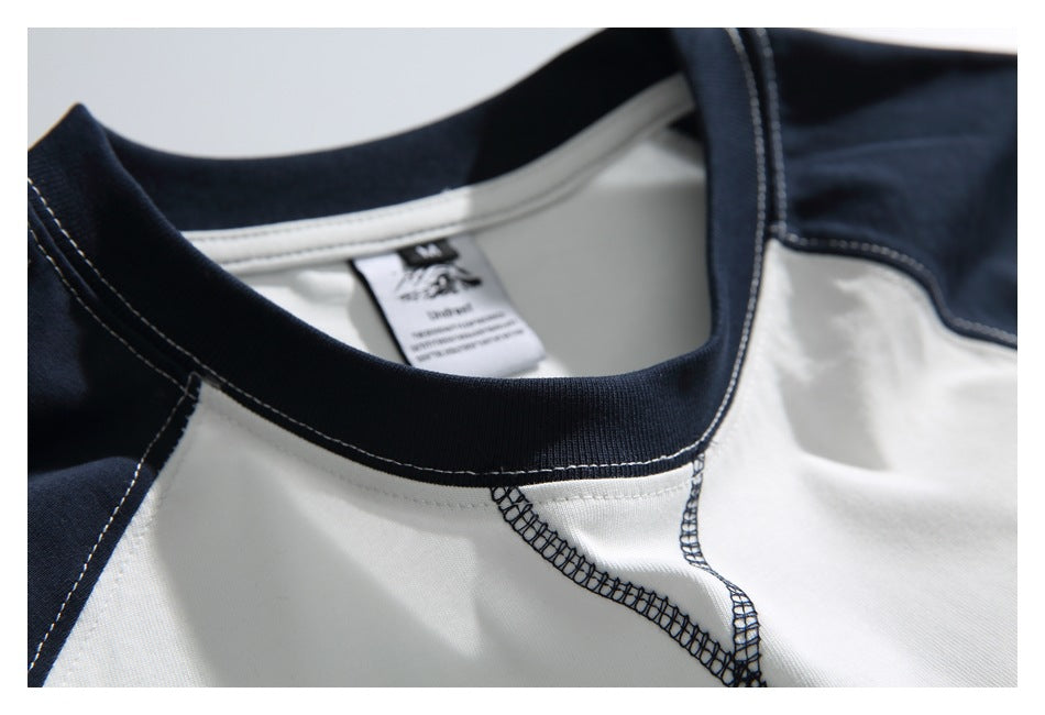 Close-up of the navy ribbed neckline, contrast seams, and inside neck label on a white raglan shirt.
