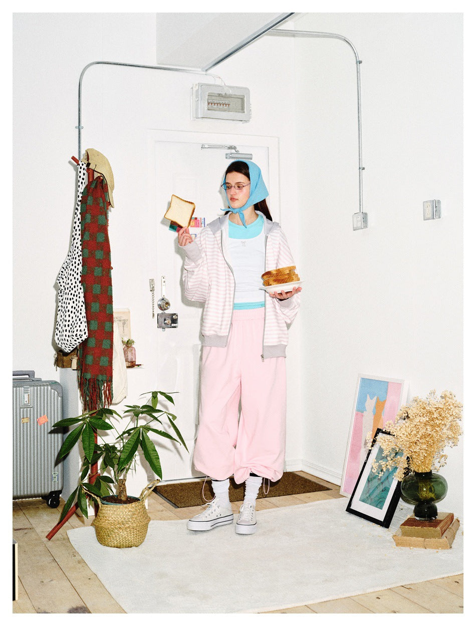 A model wears a pale pink-and-white striped zip hoodie with gray trim, shown with loose pink pants.
