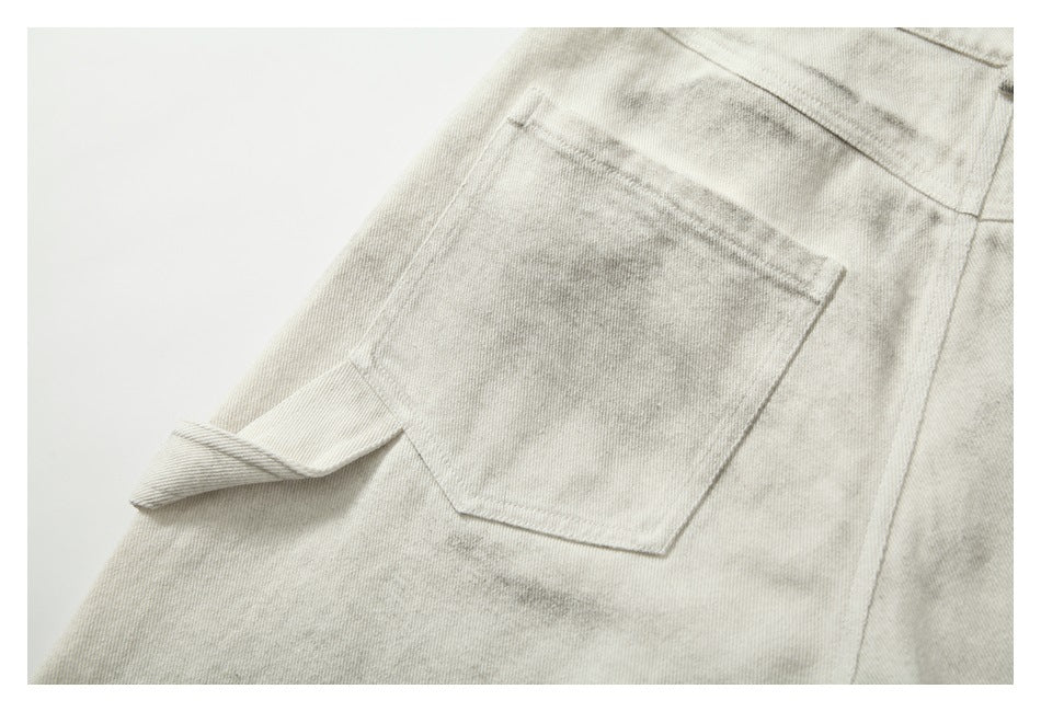 Close-up of a patch pocket and folded belt loop on cream-gray mottled trousers.