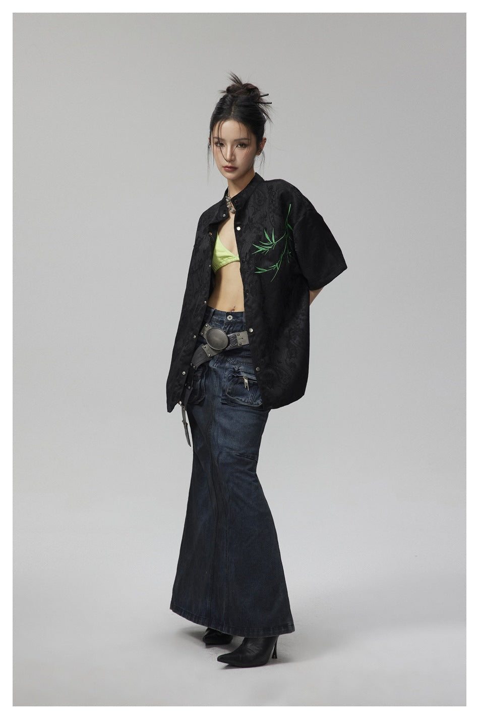 Model in a black patterned short-sleeve button-up with green branch embroidery, shown at an angle.