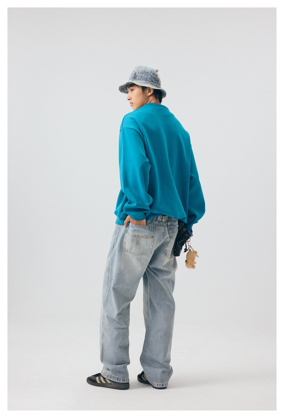 Model in a teal sweatshirt, shown from behind with light jeans and a bucket hat.