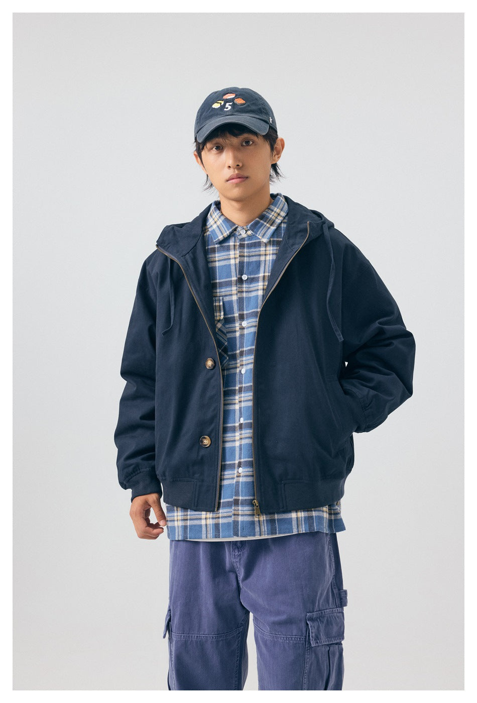 Model wearing a navy hooded jacket open over a blue plaid shirt, shown from the front.