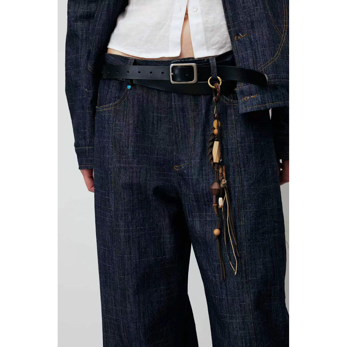 Close front view of a model wearing dark indigo wide-leg jeans, a matching jacket, and a black belt with hanging charms.