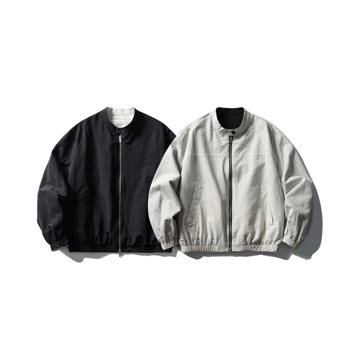 Reversible stand-collar zip jacket shown as a solid black side and a light gray pinstriped side, flat lay