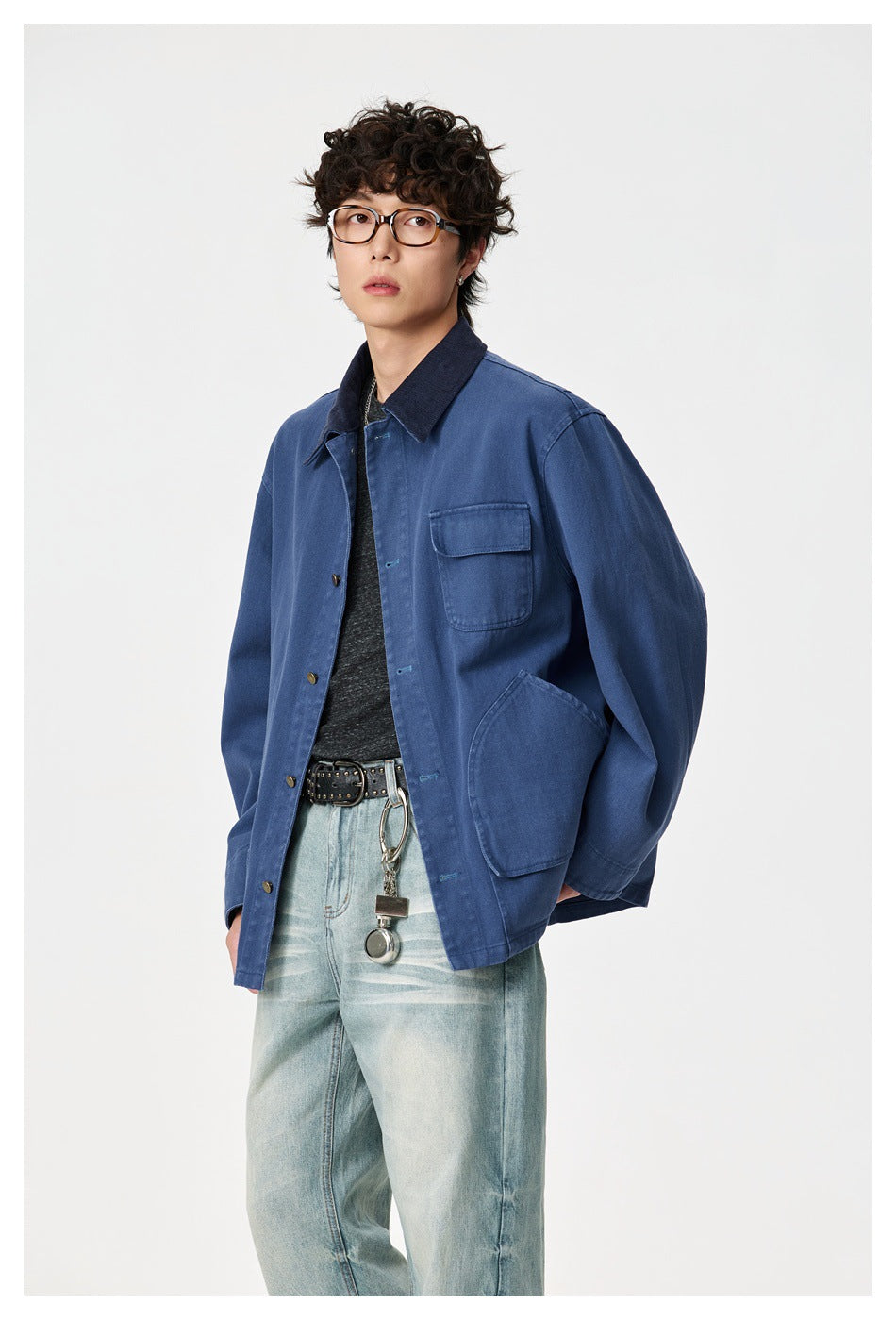 Three-quarter view of a model wearing a blue work jacket with a dark collar and multiple patch pockets.