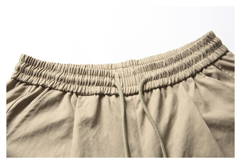 Close-up of beige shorts showing the gathered elastic waistband and long matching drawstrings.