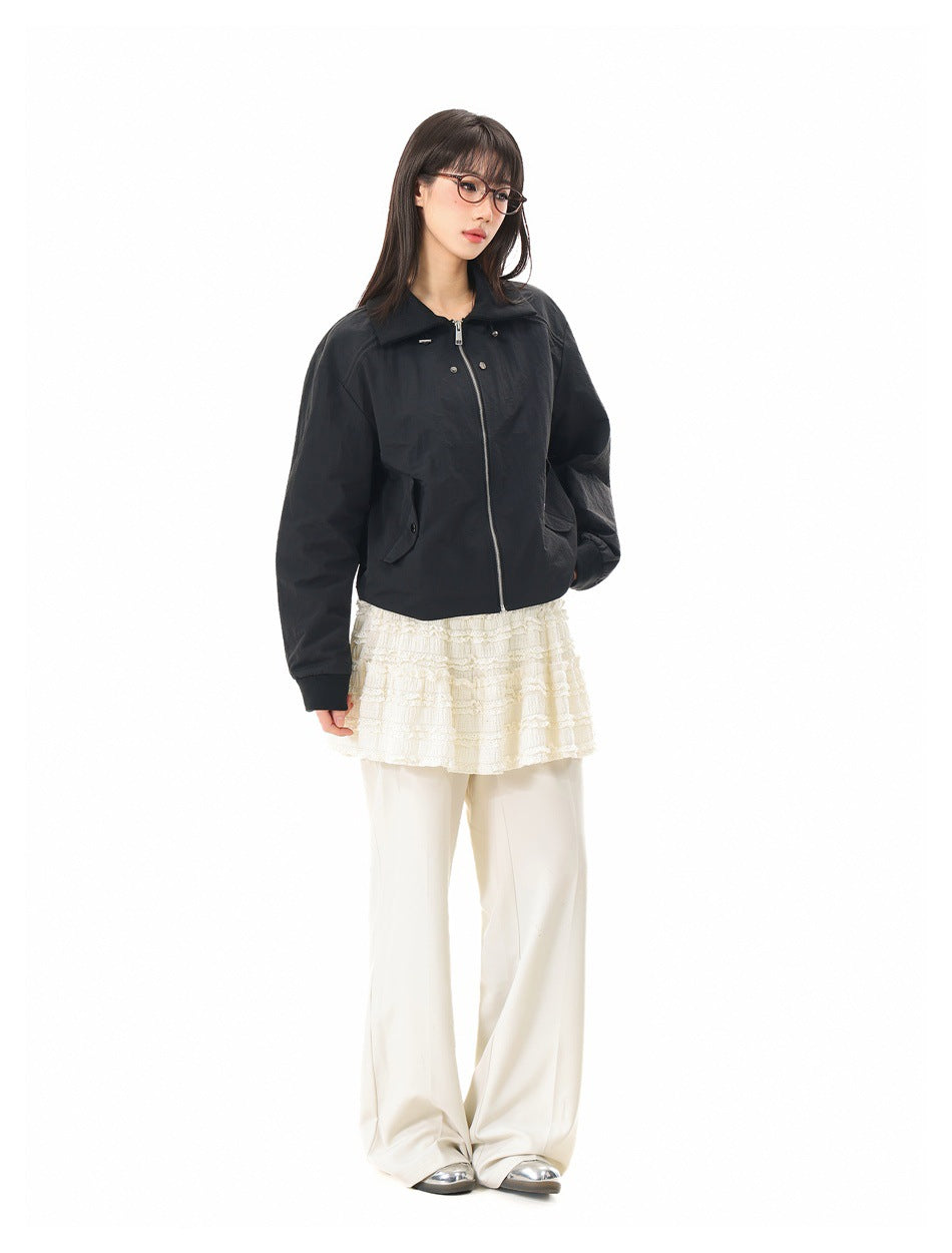 Three-quarter view of a model wearing a black collared zip jacket over a cream lace top and wide-leg trousers.