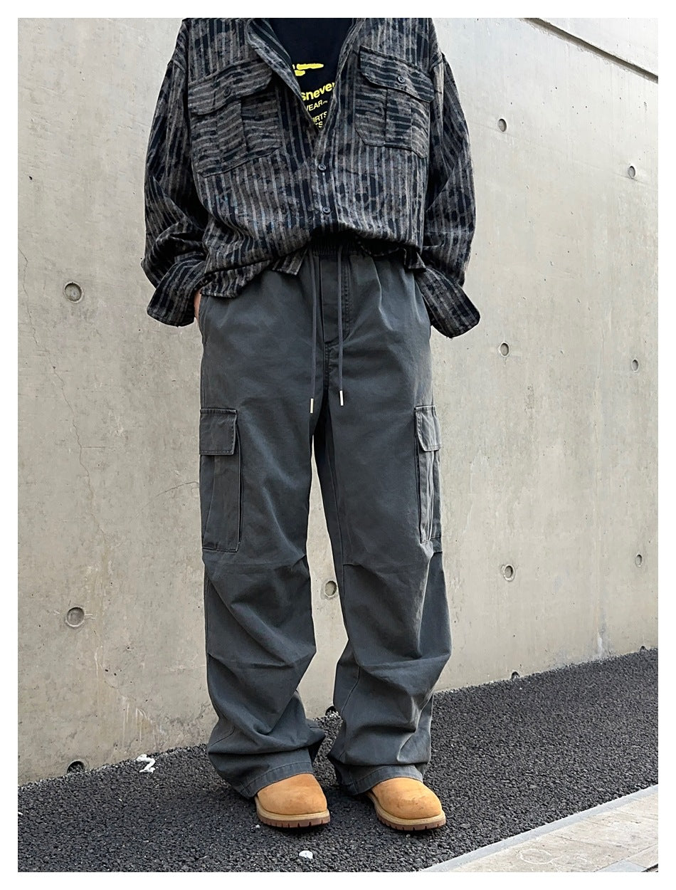 Angled view of loose charcoal cargo pants with a drawstring waist and large thigh pockets, worn with a striped shirt.