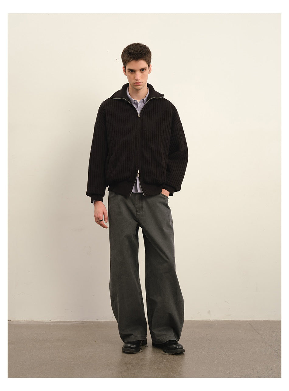 Front-facing model wearing a black ribbed zip jacket over a lavender shirt with wide charcoal trousers.