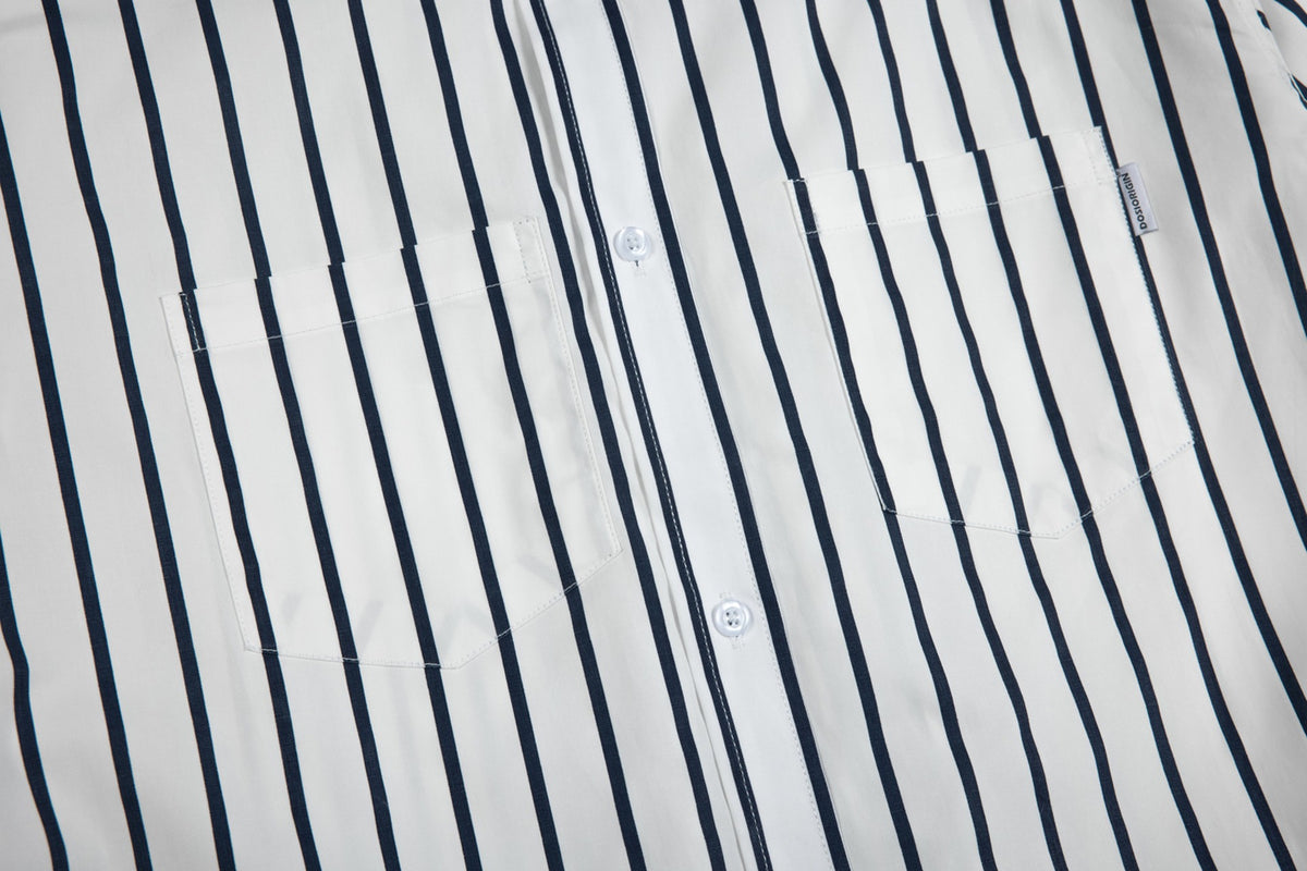 Close-up of a white shirt with navy vertical stripes, two chest pockets, white buttons, and a small side label.