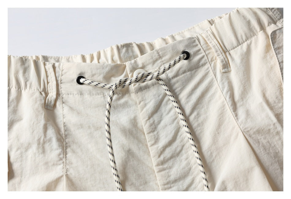 Close-up of ivory shorts with an elastic waistband, belt loops, and a black-speckled drawstring threaded through black