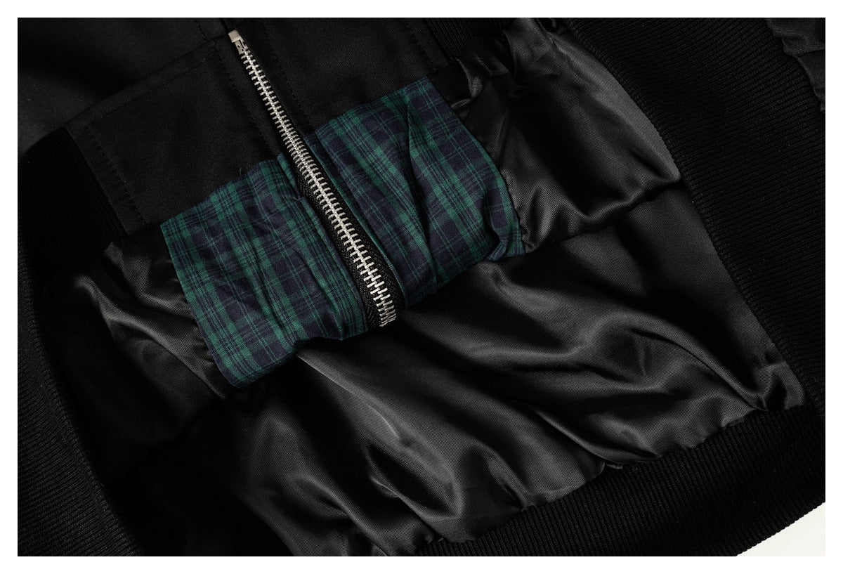 Inside of a black jacket showing a silver zipper, dark lining, and green plaid trim.