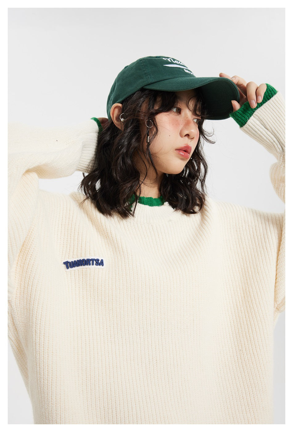 Close view of the ivory rib-knit sweater's chest patch and green-trimmed neckline and cuffs.