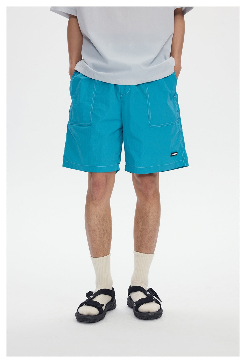Front view of a model wearing bright turquoise knee-length shorts with large front pockets and a light gray T-shirt.