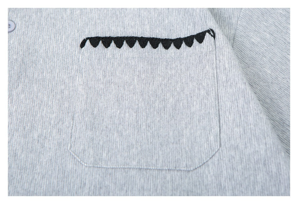 Close-up of a heather gray shirt pocket with black scalloped trim along its opening.