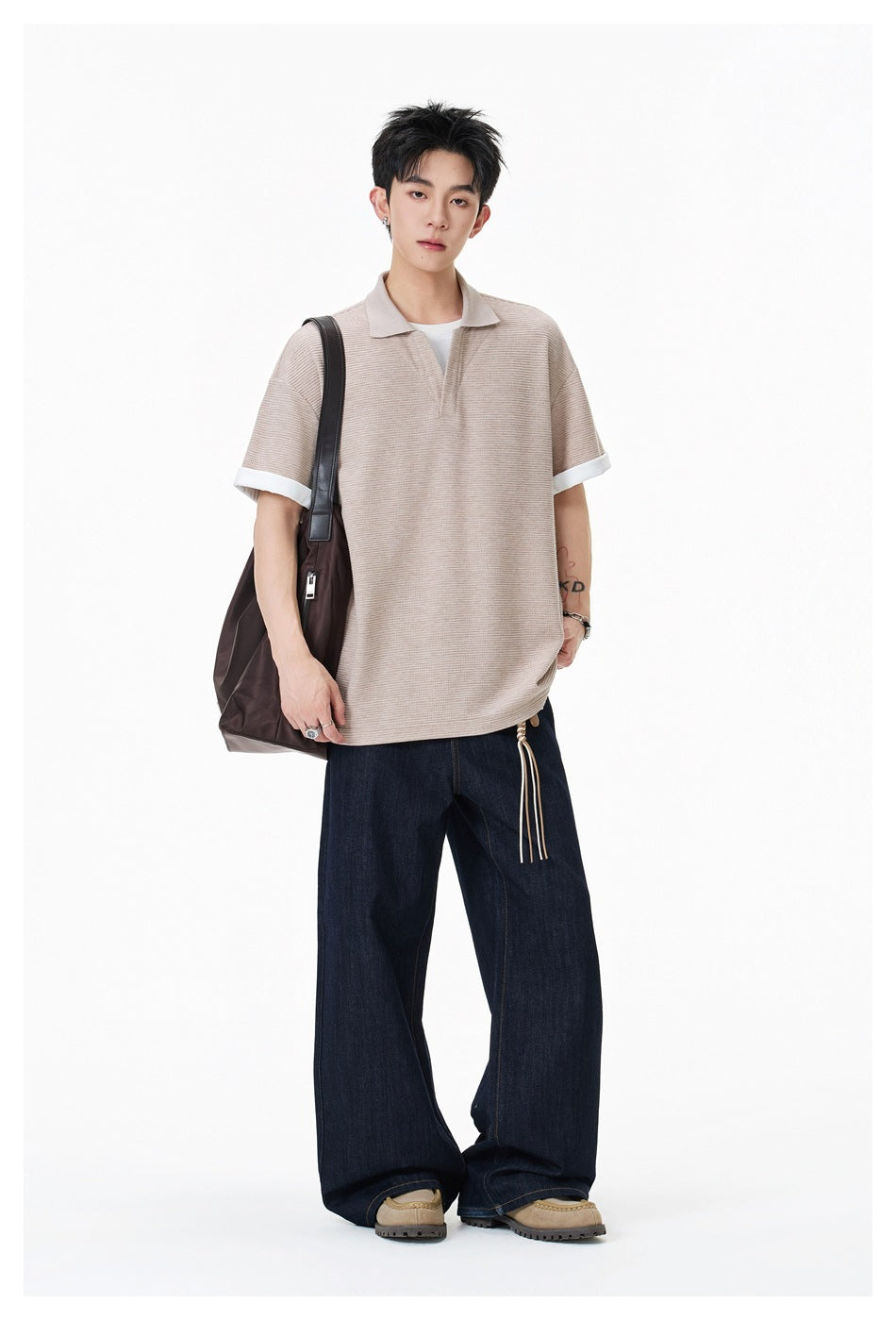 Full-length model wearing a beige textured polo, dark wide-leg jeans, and a dark shoulder bag.