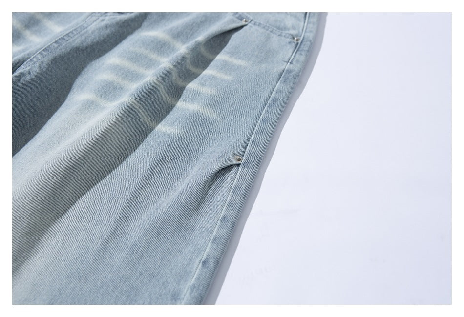 Close-up of light-wash blue denim with a diagonal seam and small metal rivets.