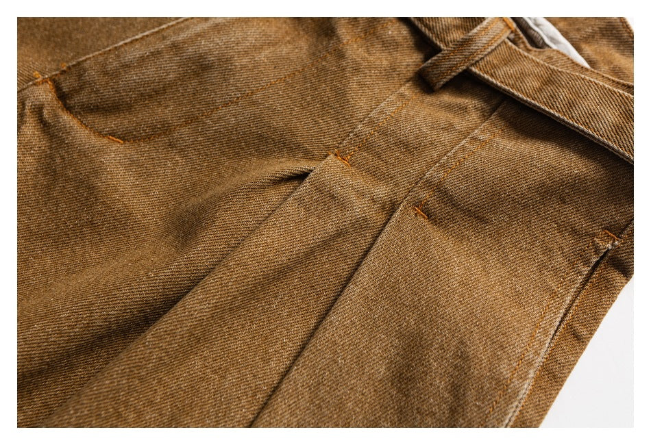 Close-up of the tan trousers' pleats, stitched seams, and belt loop.