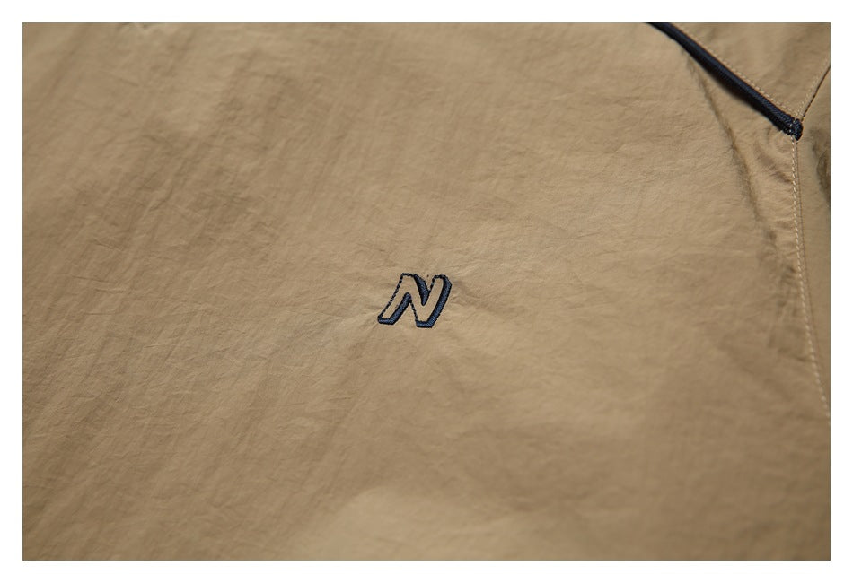 Close-up of tan fabric with a small navy embroidered letter N and part of a zip pocket.
