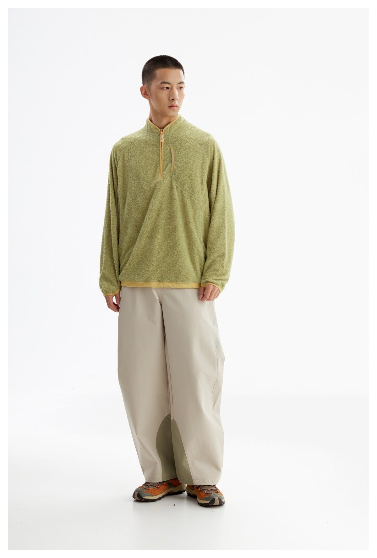 Full-length front view of a model wearing a light olive textured quarter-zip pullover with tan trim and wide beige trousers.