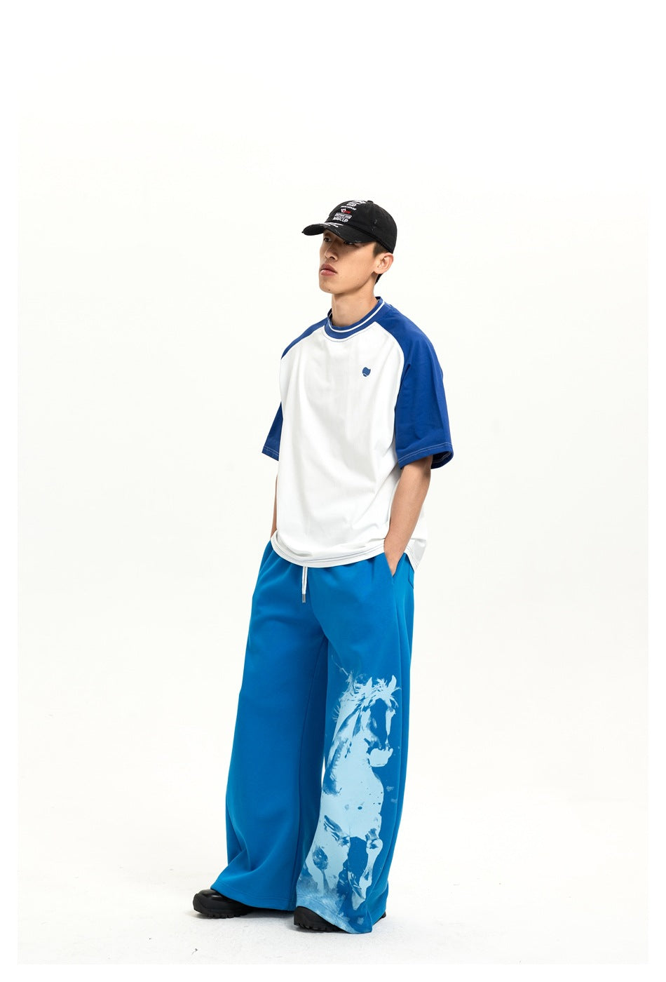 Three-quarter front view of a model in a white-and-blue raglan T-shirt and blue wide-leg pants with a horse graphic.