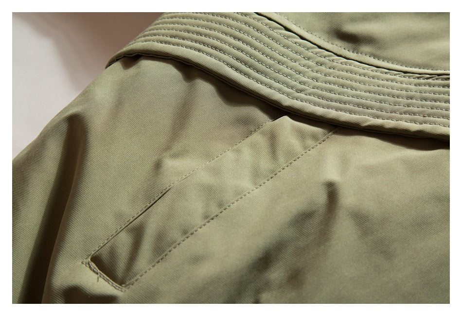 Close-up of olive-khaki garment showing a pocket opening and layered, stitched panels.