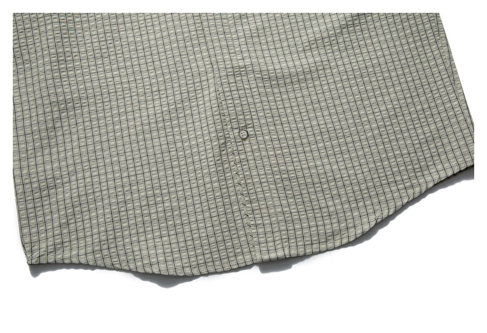 Close-up of a light gray checked shirt front showing a button and curved hem.