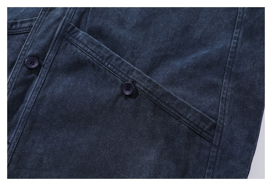 Close-up of a dark indigo garment showing a large angled pocket and two dark buttons.