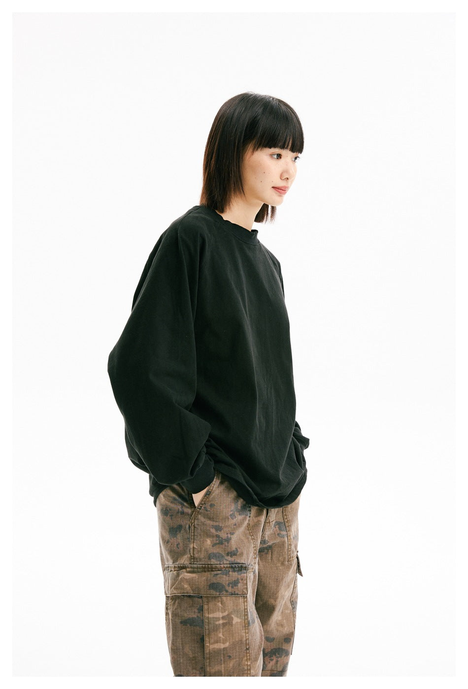 Side view of a model wearing a loose black crewneck sweatshirt and brown camouflage cargo pants.