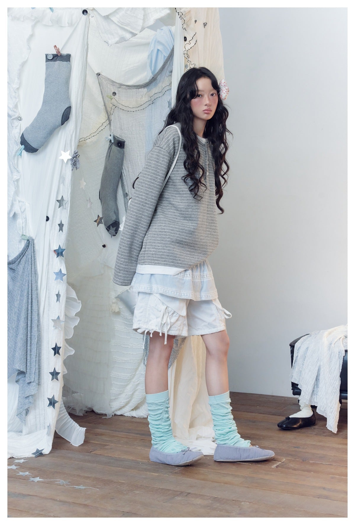 Model wearing a loose gray-and-white striped long-sleeve henley over a white layered outfit.