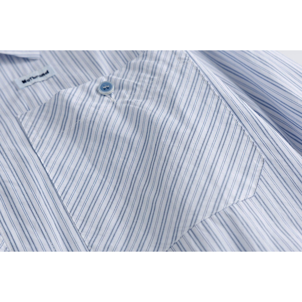 Close-up of a blue-striped shirt pocket with a blue button and a small sewn label.
