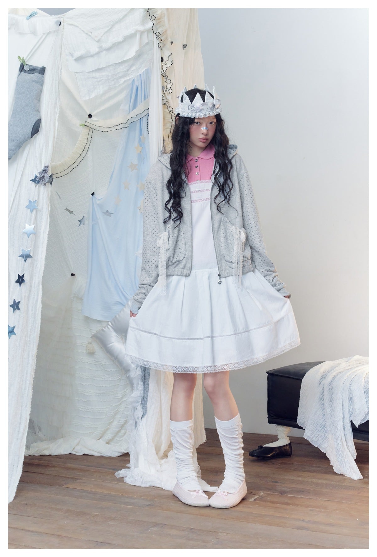 Model wearing a light gray dotted hoodie and flared white lace-hem dress, holding out the skirt.
