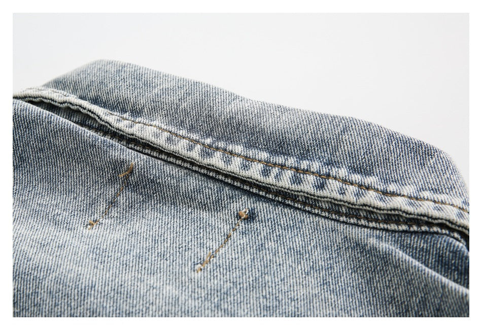 Close-up of faded blue denim with a diagonal stitched seam and two small metal rivets.