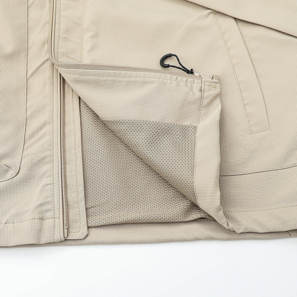 Close-up of a beige vest pocket opened to reveal mesh lining beside the front zipper.