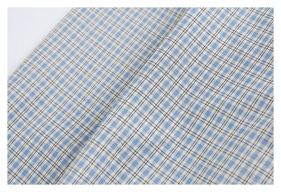 Close-up of a folded panel of light blue, white, and black plaid shirt fabric.
