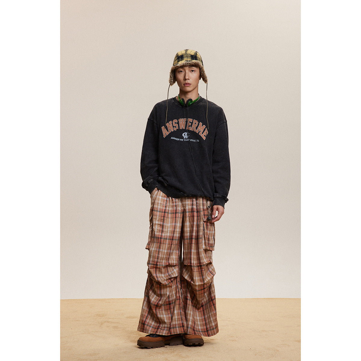 Full-length model wearing a black graphic sweatshirt and layered brown plaid cargo trousers.