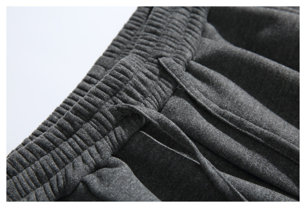 Close-up of dark gray pants with a gathered waistband, drawstring, and front pocket seam.
