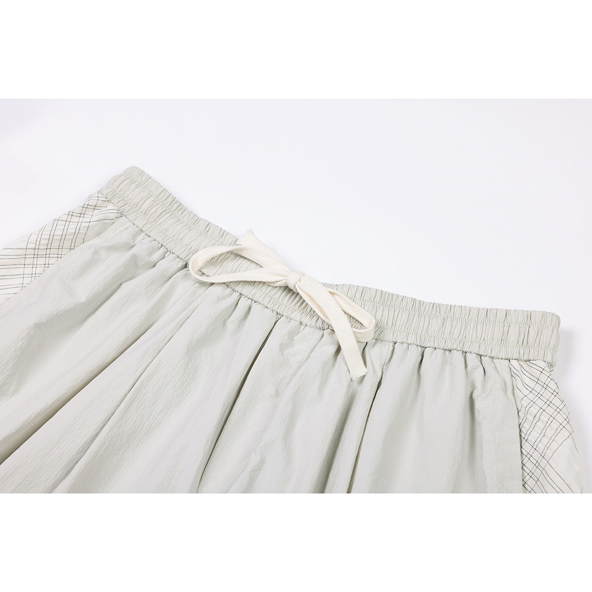 Close-up of pale gray shorts with an elastic waistband, cream drawstring, and thin plaid side panels.