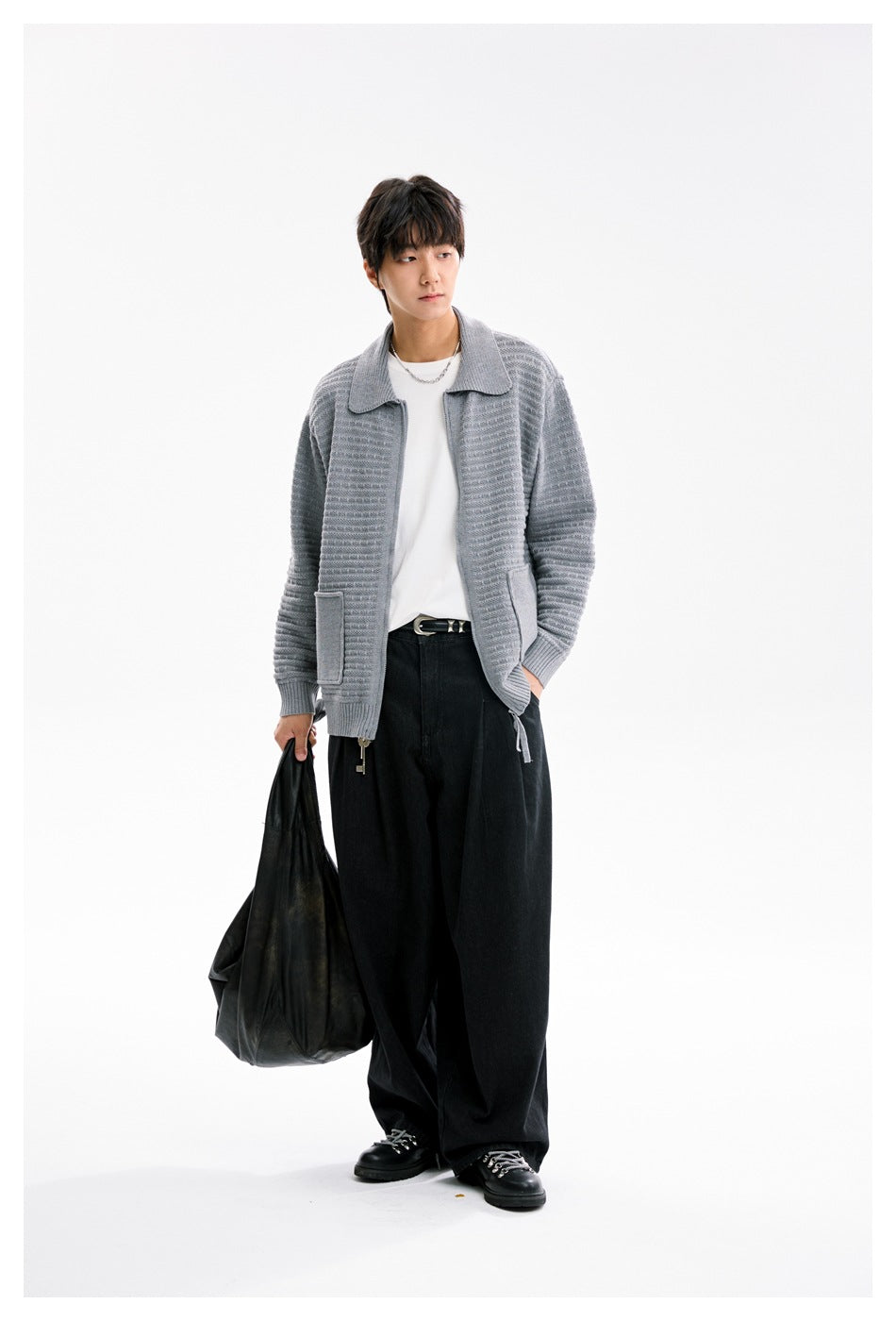 Model wearing gray knit zip cardigan over a white tee with black wide-leg pants, holding a black bag, looking aside