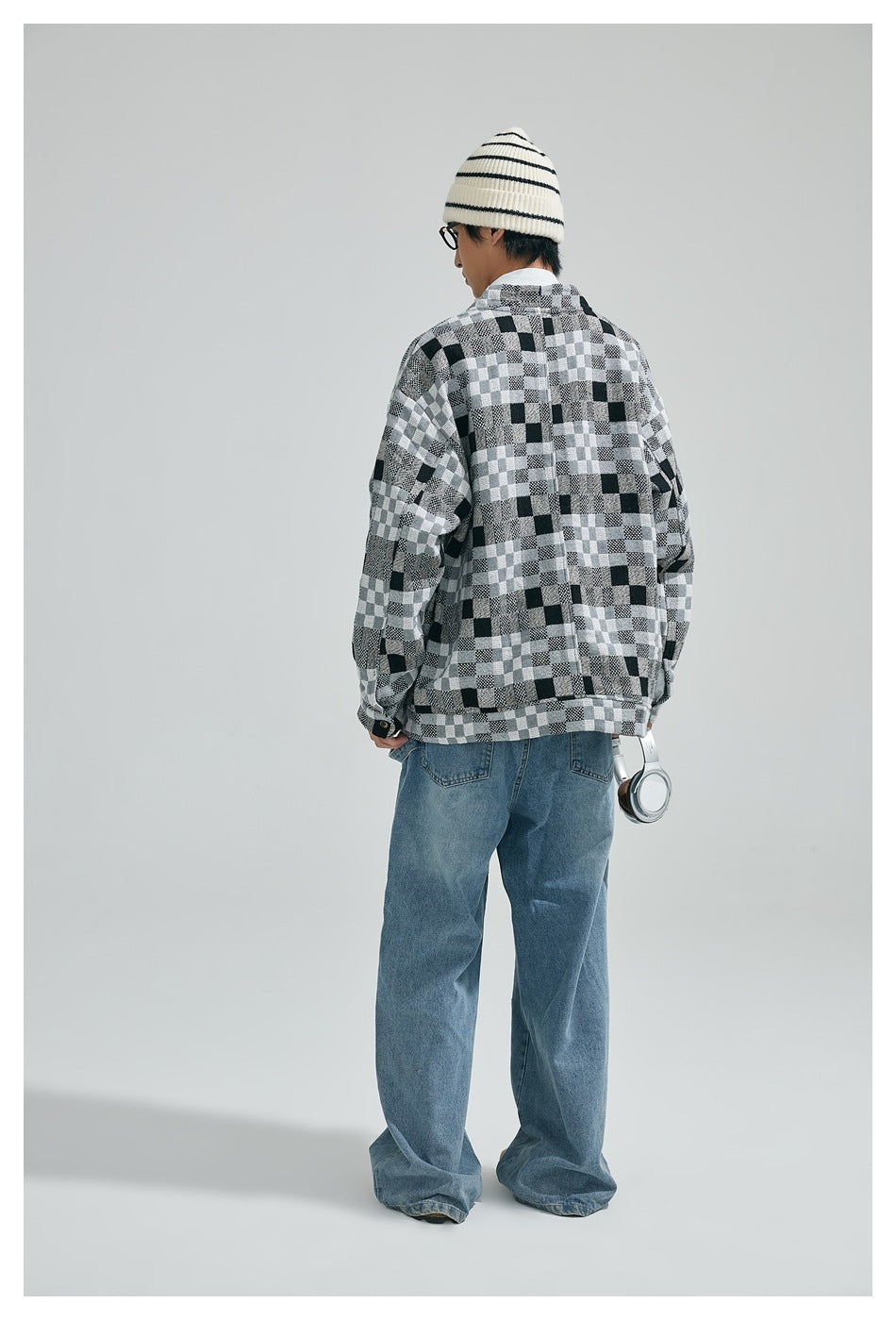 Back view of model wearing the gray checkerboard jacket with drop shoulders, beanie and wide-leg jeans