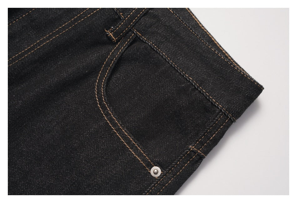 Close-up of a curved front pocket with a metal rivet on dark denim jeans.