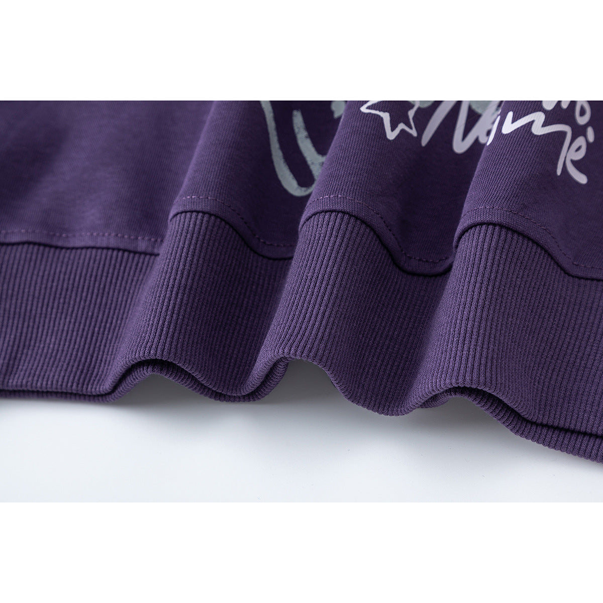 Close-up of the purple sweatshirt's ribbed hem and stitching, with part of its front graphic visible.
