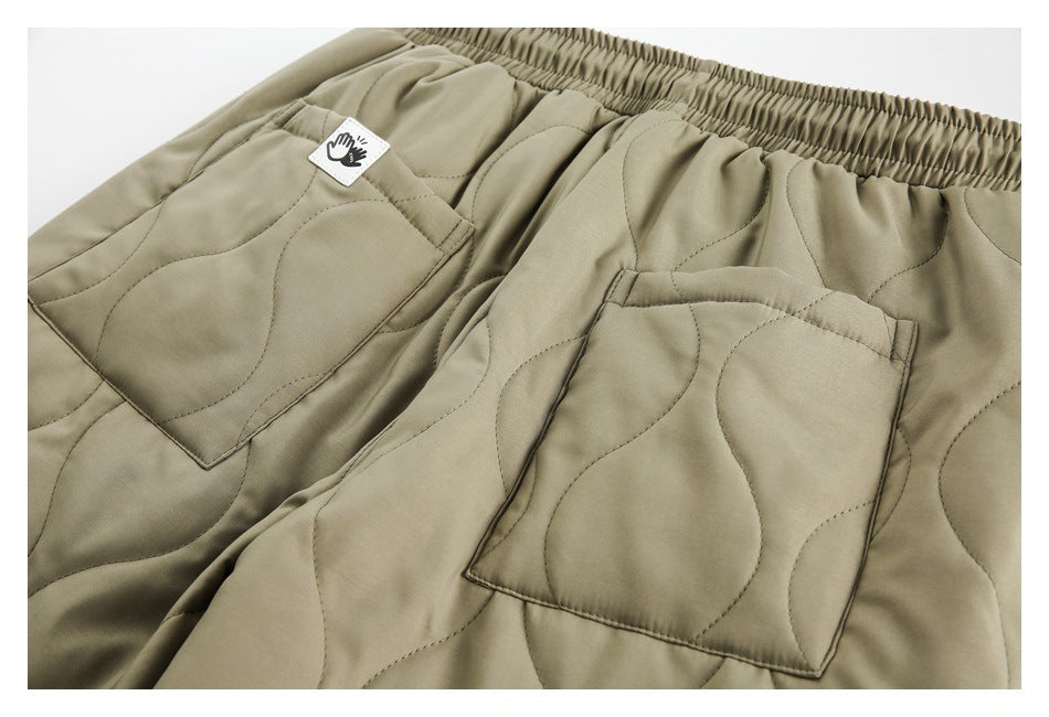 Front close-up of olive-khaki quilted trousers with an elastic waistband and two large patch pockets.