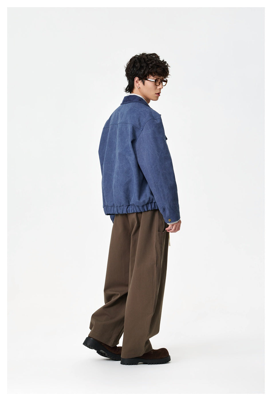 Side and back view of a model wearing a blue jacket with an elasticized hem and wide brown trousers.