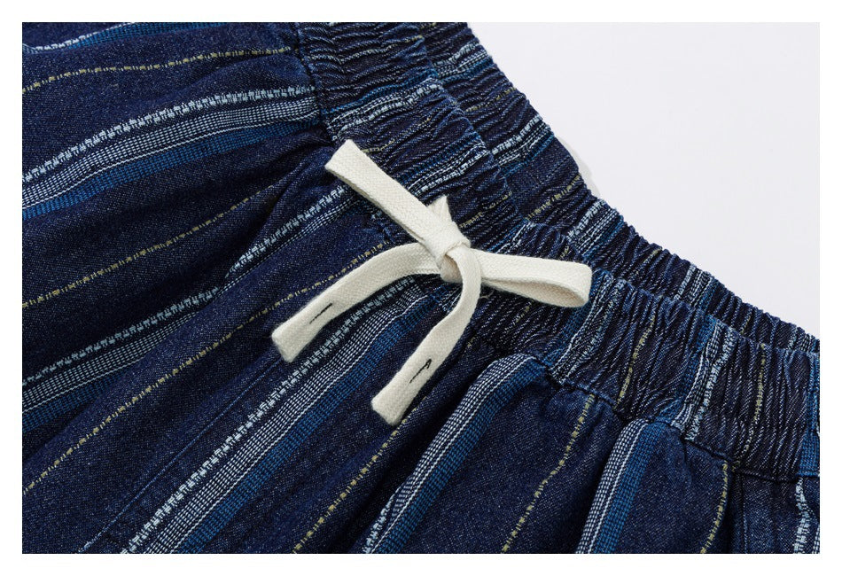 Close-up of the cream drawstring tied at the elastic waist of dark blue striped trousers.