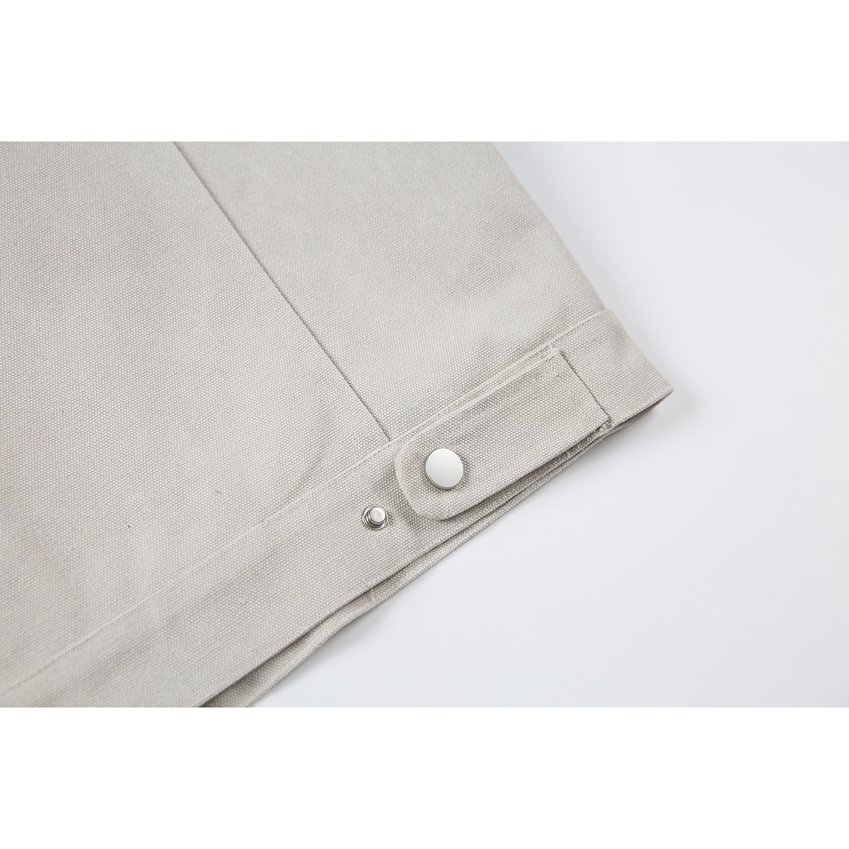 Close-up of the light beige jacket hem with a snap-fastened adjustment tab.